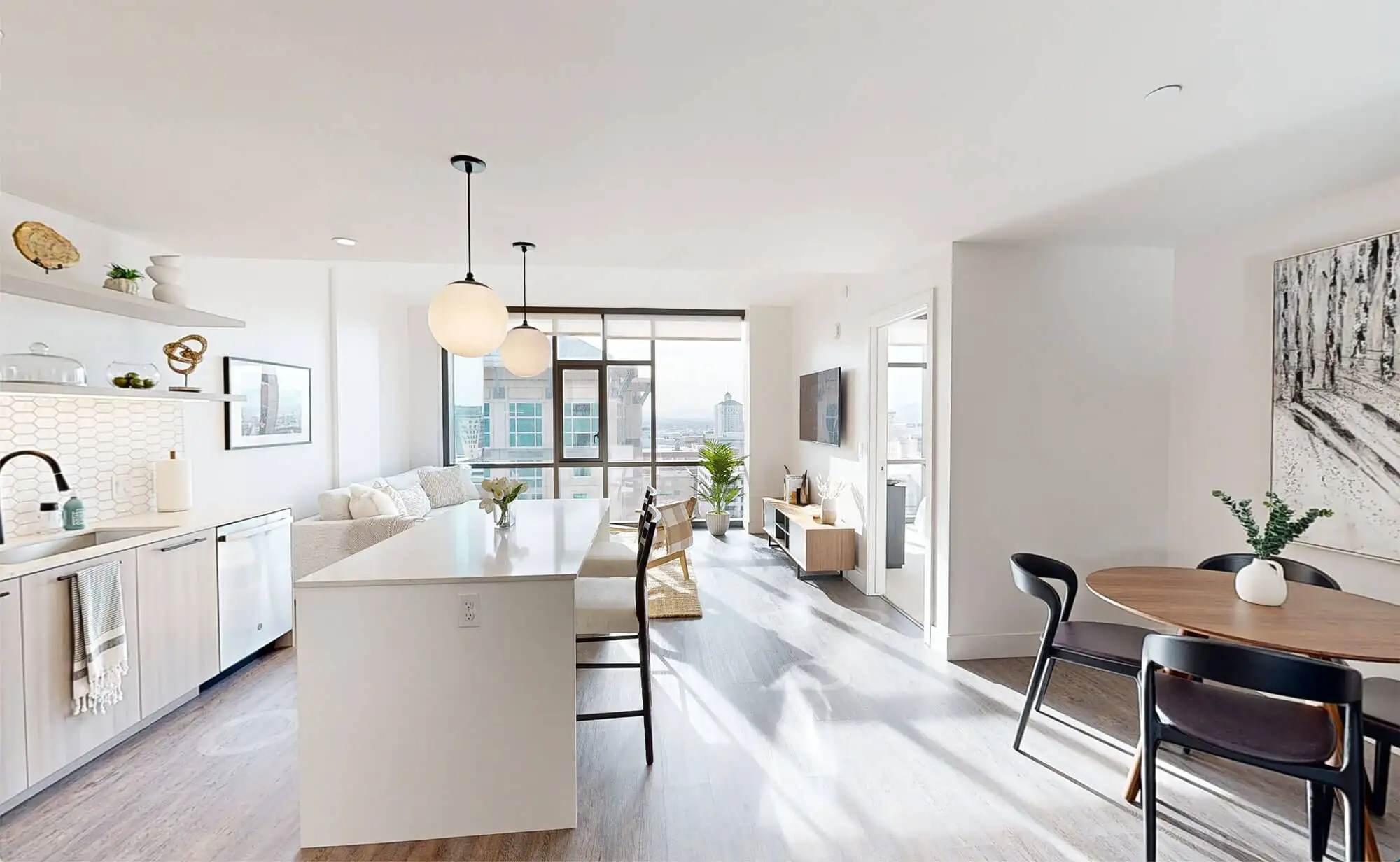 View through a 1 bedroom apartment at Astra Tower Salt Lake City, shown from the entryway to the back living room window, with kitchen on the left and dining room to the right