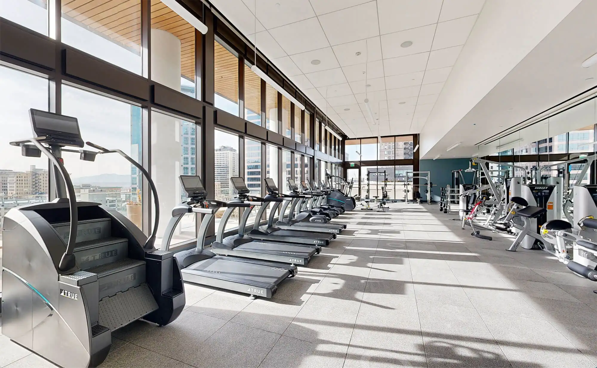 A row of treadmills and a stair climbing machine with a window view at Astra Tower Salt Lake City Apartments